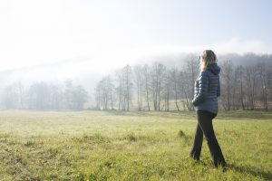 Woman walks through hilly meadow in mist